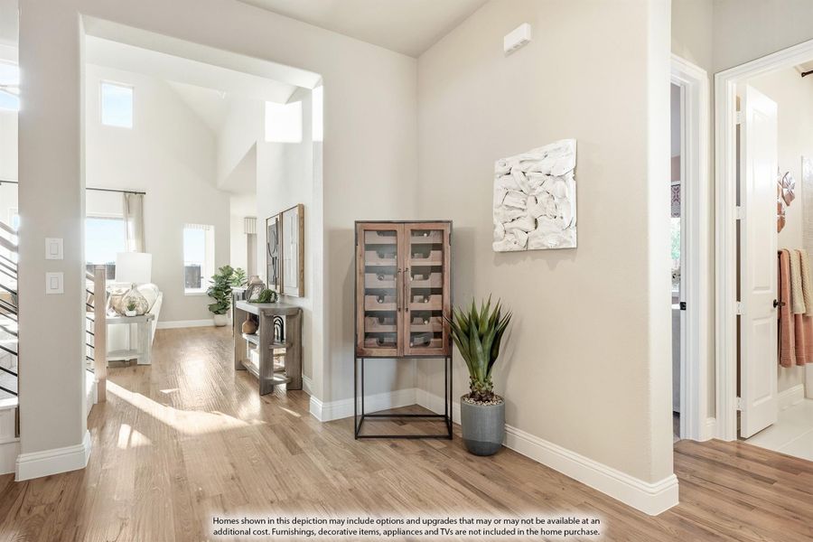 Open entryway with hardwood floors, high ceilings, and a wood wine cabinet next to a potted plant Open entryway with hardwood floors, high ceilings, and a wood wine cabinet next to a potted plant