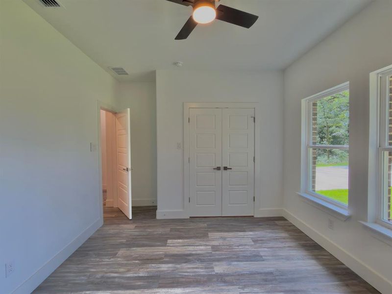 Spacious room featuring wood-finish flooring, crisp white walls, and a ceiling fan with integrated lighting
