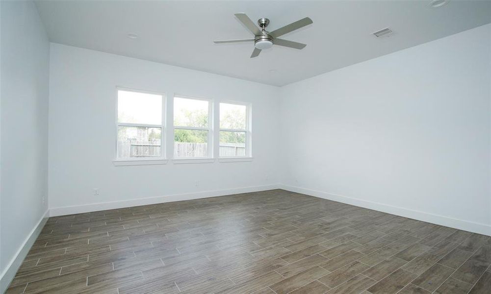 This is a bright primary bedroom with fresh neutral paint, three large windows for ample natural light, modern wood-look flooring, and a ceiling fan, offering a clean canvas for personalization.