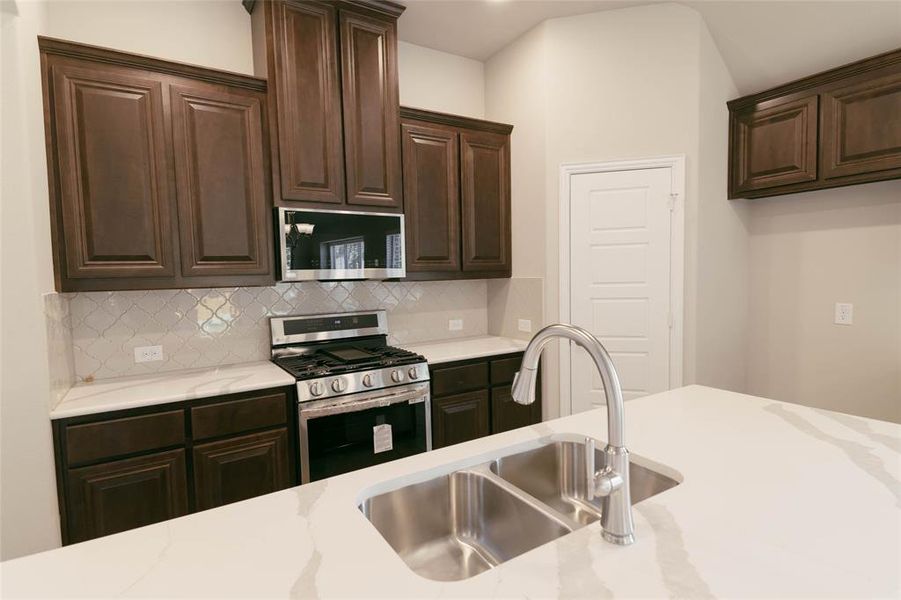 Kitchen featuring backsplash, appliances with stainless steel finishes, sink, light stone counters, and dark brown cabinetry