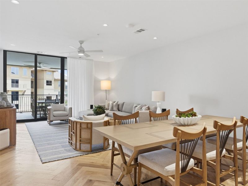 Open-concept living and dining area featuring herringbone wood-finish flooring, recessed lighting, and a private balcony with black metal railings Open-concept living and dining area featuring herringbone wood-finish flooring, recessed lighting, and a private balcony with black metal railings
