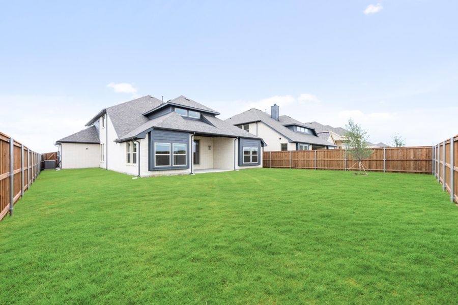 Backyard of a single-story home with large green lawn, wood privacy fence, and covered patio area.