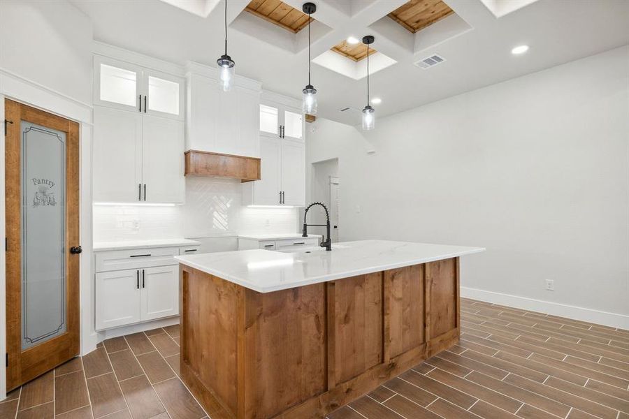 Kitchen with white cabinetry, sink, decorative light fixtures, and an island with sink