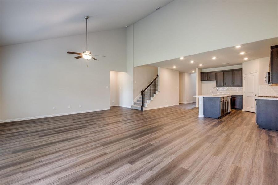 Unfurnished living room featuring ceiling fan, sink, light wood-type flooring, and high vaulted ceiling