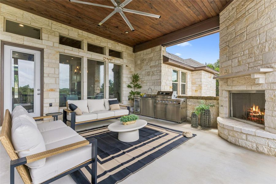 An inviting outdoor living space features a built-in fireplace, a full outdoor kitchen, and comfortable seating for entertaining.