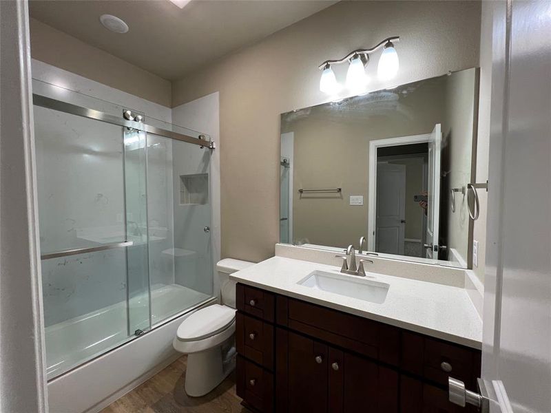 Full bathroom featuring hardwood / wood-style floors, vanity, enclosed tub / shower combo, and toilet