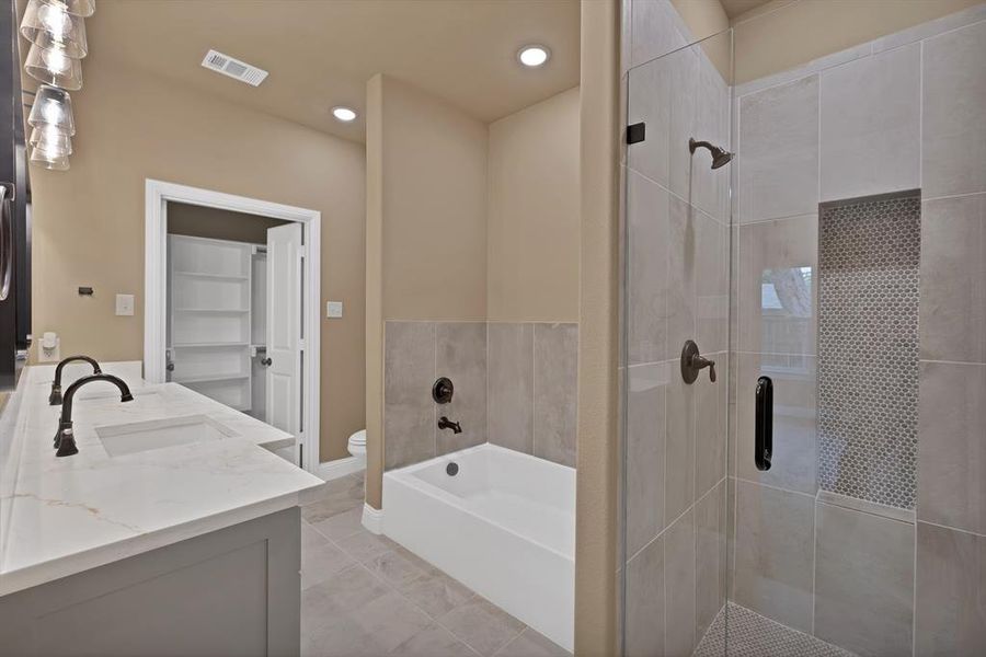 Full bathroom featuring visible vents, toilet, a sink, a bath, and a stall shower Full bathroom featuring visible vents, toilet, a sink, a bath, and a stall shower