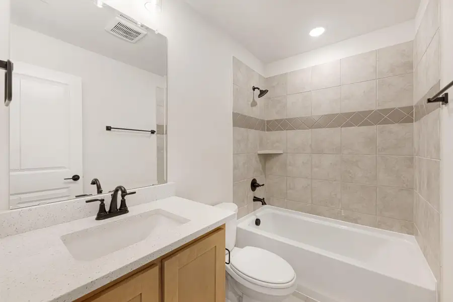 Bathroom with quartz vanity, wood cabinets, and tiled shower-tub combo with dark bronze fixtures
