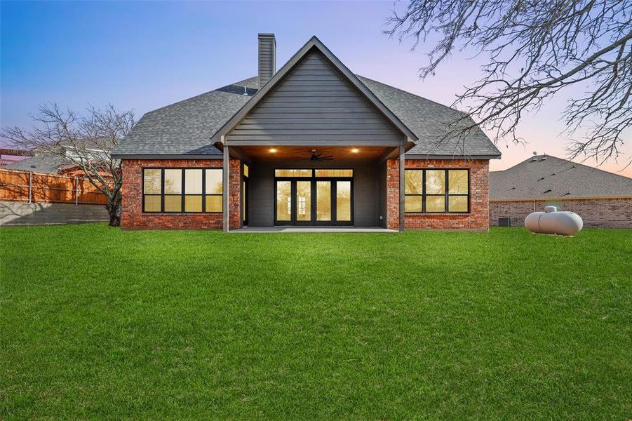 Back house at dusk with a lawn, a patio, and ceiling fan