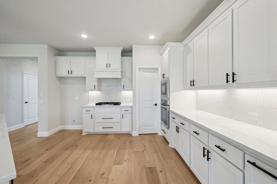 Kitchen with stainless steel appliances, decorative backsplash, white cabinetry, light wood finished floors, and recessed lighting