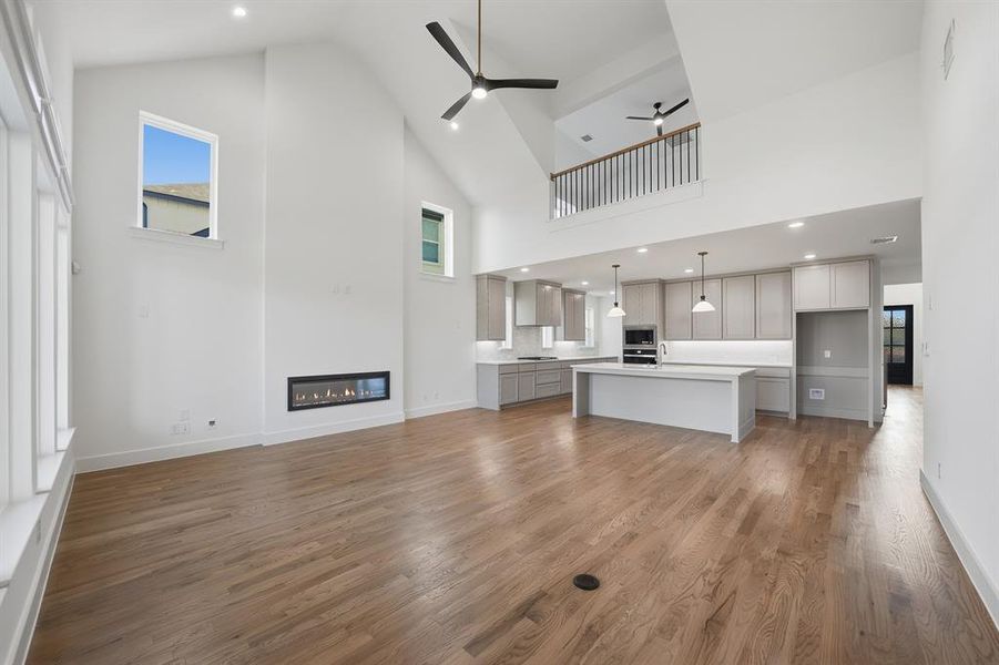 Unfurnished living room with high vaulted ceiling, a glass covered fireplace, a ceiling fan, dark wood finished floors, and recessed lighting Unfurnished living room with high vaulted ceiling, a glass covered fireplace, a ceiling fan, dark wood finished floors, and recessed lighting