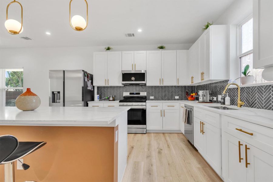 Kitchen with stainless steel appliances, light stone countertops, and white cabinets