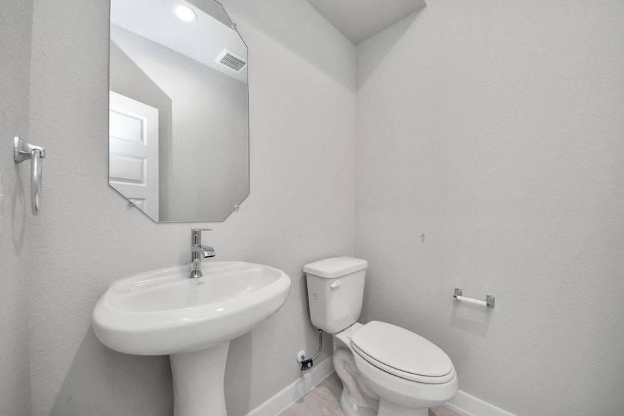 This half bathroom features a stylish pedestal sink, modern hardware, and bright recessed lighting, creating a sleek and inviting space. Sample photo of completed home with similar floor plan. Actual colors and selections may vary. This half bathroom features a stylish pedestal sink, modern hardware, and bright recessed lighting, creating a sleek and inviting space. Sample photo of completed home with similar floor plan. Actual colors and selections may vary.