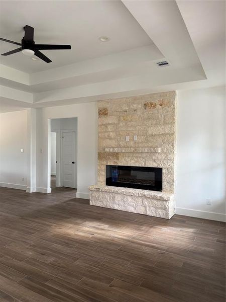 This is a spacious room featuring a modern electric fireplace with a stone surround, elegant hardwood flooring, and a high ceiling with a sleek ceiling fan. It includes ample natural light and a clean, contemporary design.