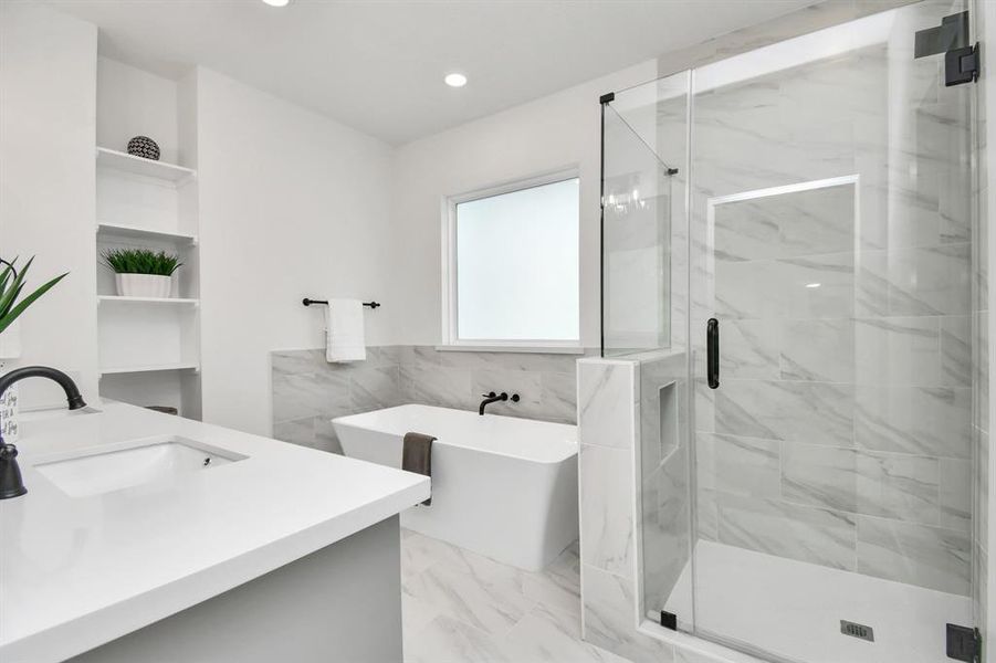 A breathtaking view of the primary bathroom with frameless shower and stand alone tub with accent shelves.