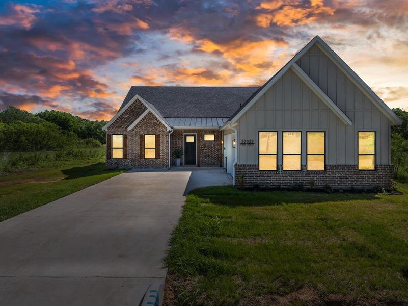 View of front of house with concrete driveway, brick siding, board and batten siding, a front lawn, and roof with shingles