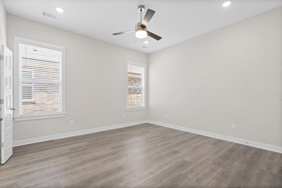 Wood-finish flooring, two windows with blinds, recessed lighting, and a ceiling fan with integrated lighting
