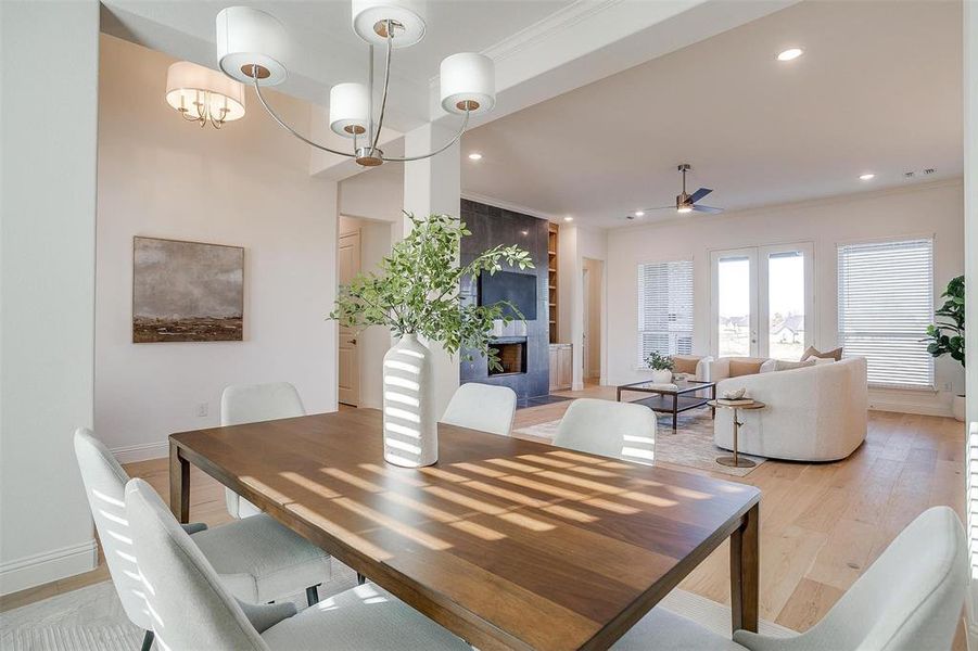 Dining area featuring ceiling fan with notable chandelier, light hardwood / wood-style floors, ornamental molding, and a tiled fireplace