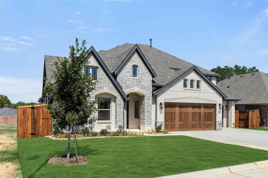 Two-story stone and brick home with two-car garage, arched entry, and manicured front lawn