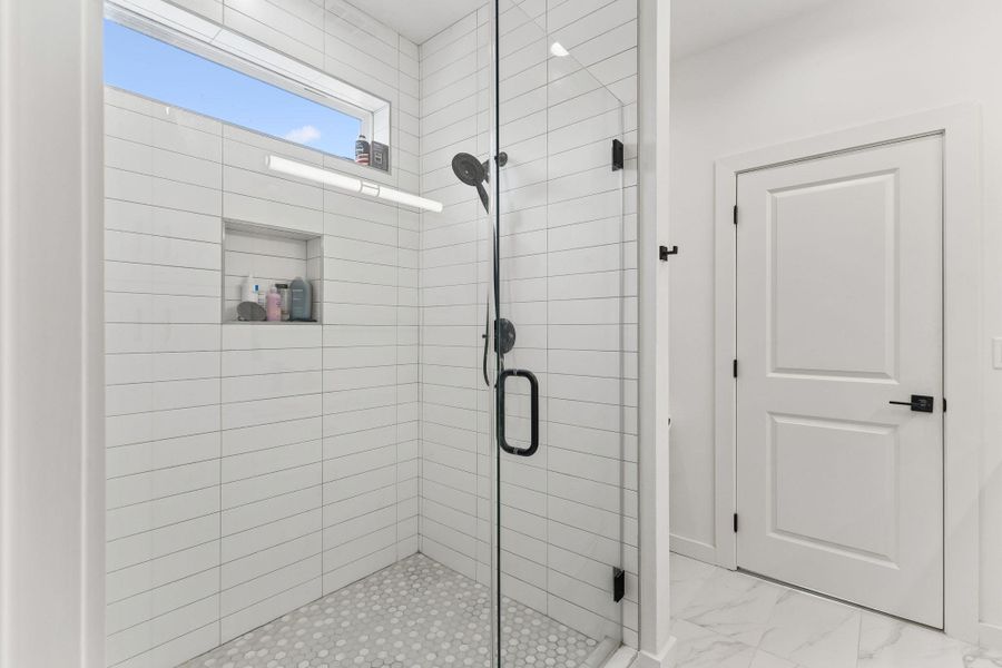 Glass-enclosed shower featuring white subway tile, a built-in shower niche, and a contrasting pebble tile floor