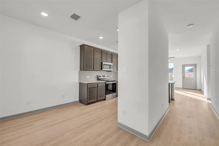Kitchen with dark wood finish cabinetry, stainless steel appliances, light wood-style floors, decorative backsplash, and recessed lighting
