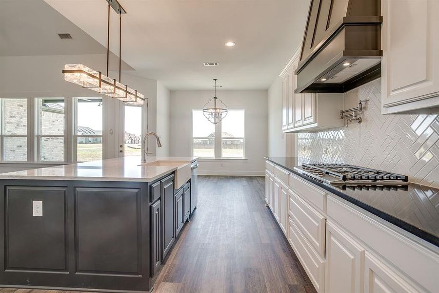 Kitchen featuring two tone cabinets, dark stone counters, a large island with sink, dark wood-style flooring, and a chandelier Kitchen featuring two tone cabinets, dark stone counters, a large island with sink, dark wood-style flooring, and a chandelier