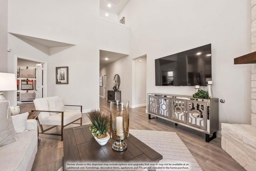 Living room with two-story ceiling, hardwood floors, stone fireplace, and wall-mounted TV above mirrored console table.