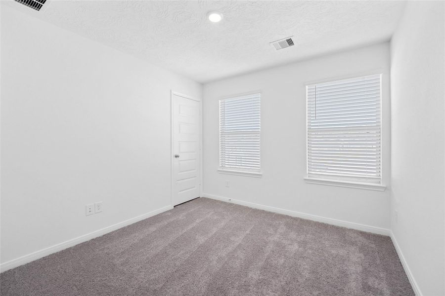 Secondary bedroom features plush carpet, neutral paint, lighting, large windows with privacy blinds, and a walk-in closet.