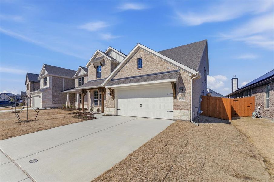 View of front facade featuring stone siding, driveway, covered porch, a gate, and a garage