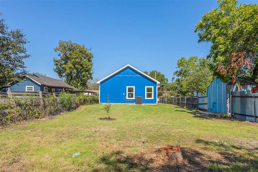 Spacious backyard featuring a vibrant blue exterior, white trim windows, and mature trees