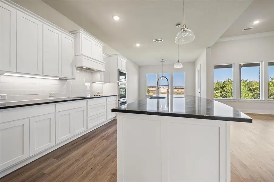 Kitchen featuring backsplash, white cabinets, a kitchen island with sink, pendant lighting, and recessed lighting Kitchen featuring backsplash, white cabinets, a kitchen island with sink, pendant lighting, and recessed lighting