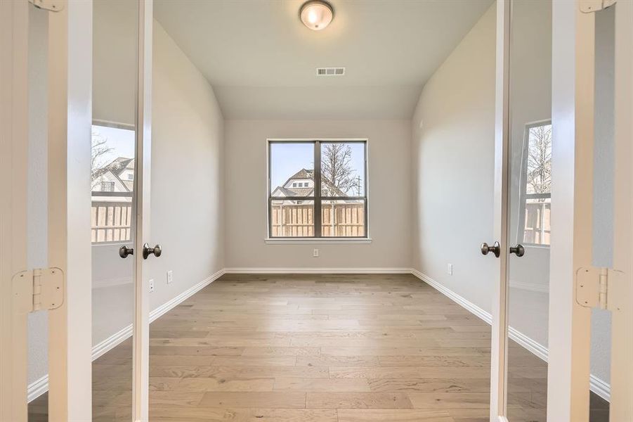 Spare room with light hardwood / wood-style floors, lofted ceiling, and french doors