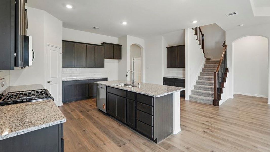 Open-concept kitchen featuring an island with a double sink, stainless steel dishwasher, granite countertops, dark wood-finish cabinetry, and wood-finish flooring