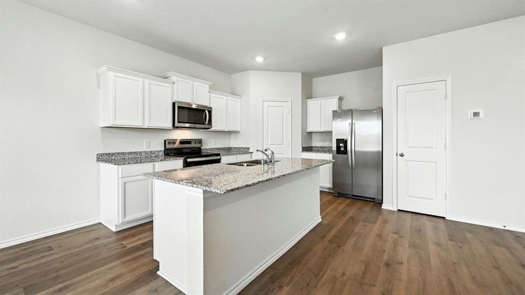 Kitchen featuring an island with a built-in sink, white cabinetry, granite countertops, and stainless steel appliances