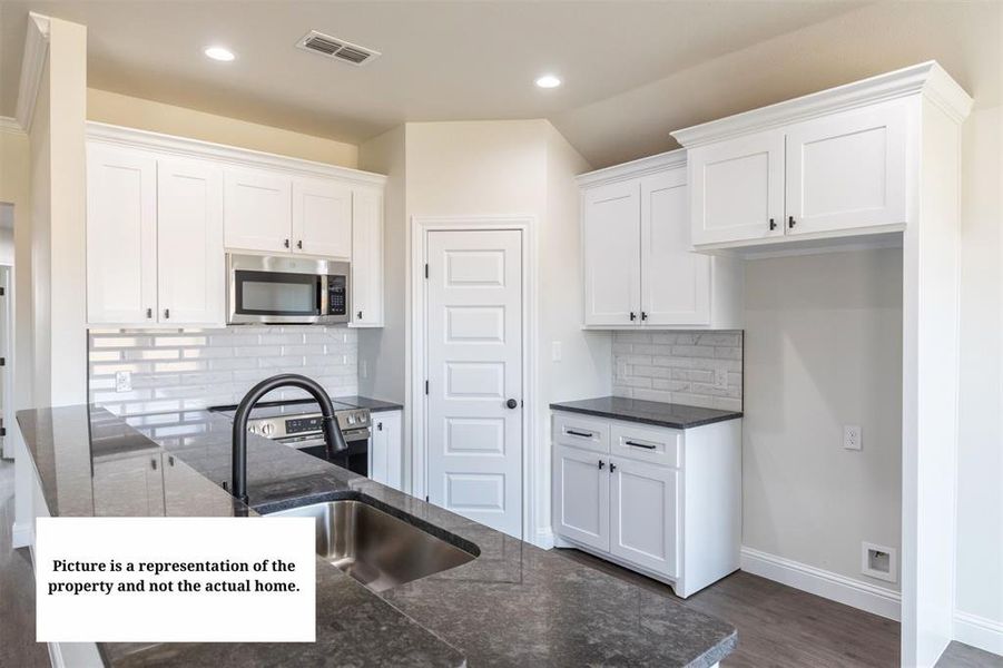 Kitchen featuring white shaker-style cabinetry, dark granite countertops, stainless steel appliances, a subway tile backsplash, and a large island with an undermount sink and matte black faucet
