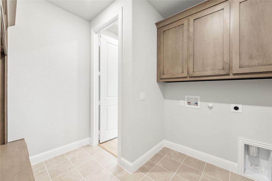 Laundry room with upper wood cabinets, washer and dryer hookups, and light tile flooring Laundry room with upper wood cabinets, washer and dryer hookups, and light tile flooring