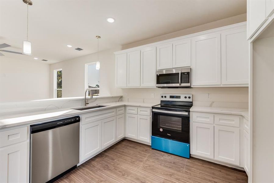 Kitchen featuring stainless steel appliances, light hardwood / wood-style floors, sink, decorative light fixtures, and white cabinets