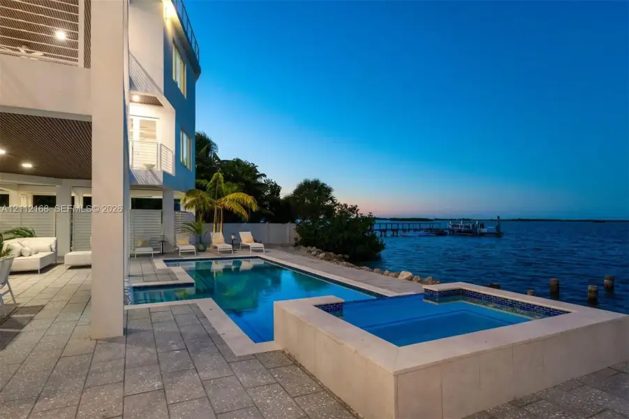 Waterfront patio featuring a concrete paver deck, built-in swimming pool, elevated spa, and multi-level balconies Waterfront patio featuring a concrete paver deck, built-in swimming pool, elevated spa, and multi-level balconies