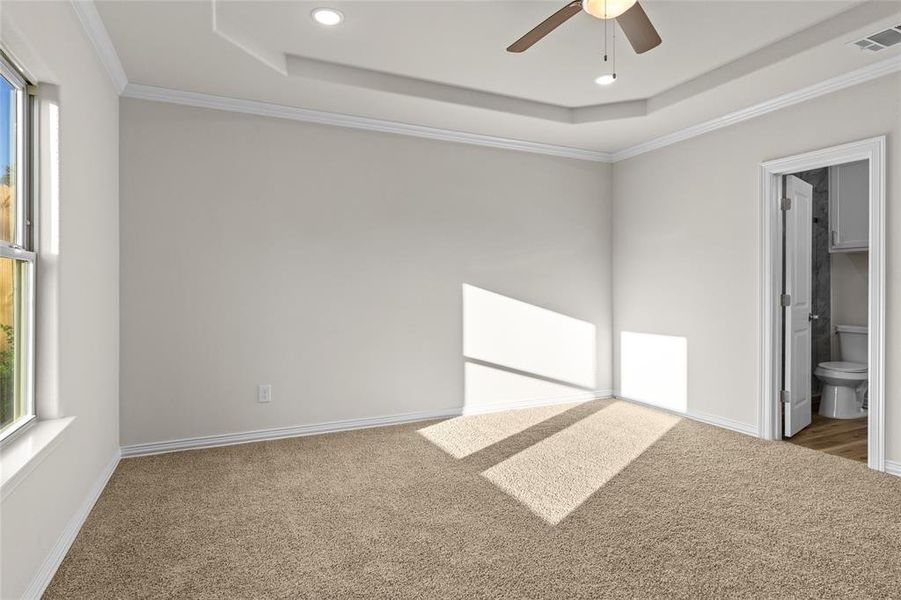 Unfurnished bedroom featuring a tray ceiling, ornamental molding, carpet floors, ensuite bath, and ceiling fan