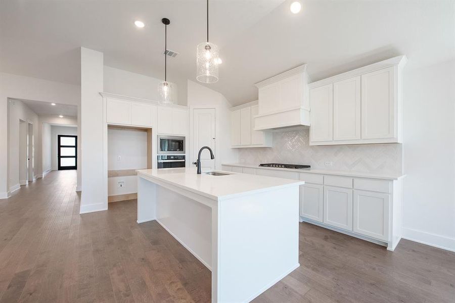 Kitchen with decorative backsplash, white cabinets, light wood finished floors, hanging light fixtures, and lofted ceiling Kitchen with decorative backsplash, white cabinets, light wood finished floors, hanging light fixtures, and lofted ceiling
