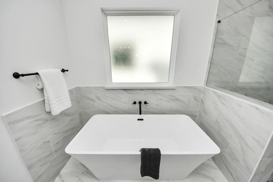 This bathroom features a modern, freestanding bathtub with sleek black fixtures and elegant gray marble tile. A frosted window provides privacy and natural light, while a towel rack adds convenience.