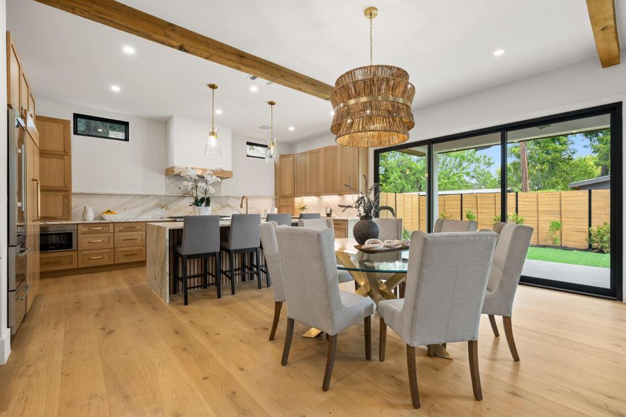 Exposed ceiling beams accent this open kitchen and dining area with wide-plank flooring.
