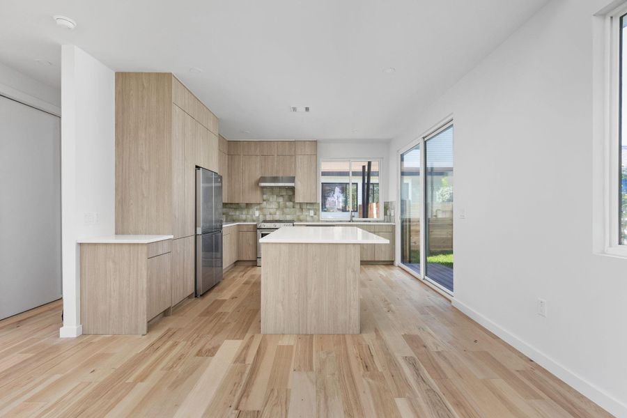 Kitchen featuring stainless steel appliances, light brown cabinets, exhaust hood, modern cabinets, and light countertops