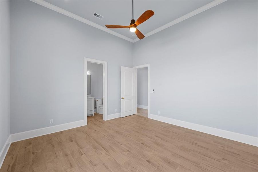 Unfurnished bedroom with wood finished floors, a ceiling fan, connected bathroom, a high ceiling, and ornamental molding Unfurnished bedroom with wood finished floors, a ceiling fan, connected bathroom, a high ceiling, and ornamental molding