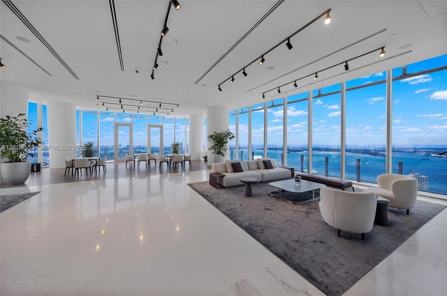 Expansive open-concept floor plan featuring floor-to-ceiling glass walls, polished stone flooring, industrial-style track lighting, and structural columns
