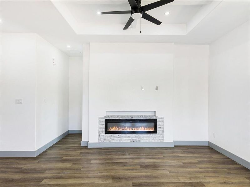 Unfurnished living room with a tray ceiling, a glass covered fireplace, dark wood-type flooring, recessed lighting, and ceiling fan Unfurnished living room with a tray ceiling, a glass covered fireplace, dark wood-type flooring, recessed lighting, and ceiling fan