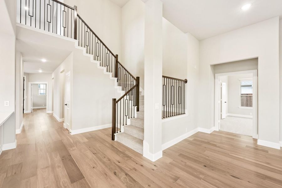 Open foyer with two-story staircase, dark iron balusters, and light hardwood floors