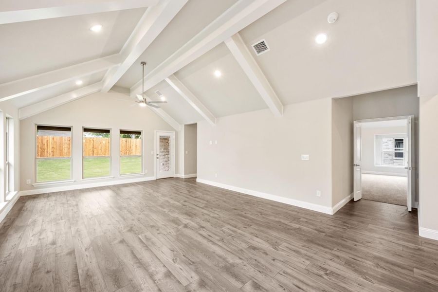 Open living room with vaulted ceiling, white exposed beams, ceiling fan, and light wood floors