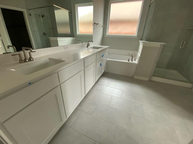 Double vanity with white cabinetry, integrated sinks, brushed nickel fixtures, and a spacious mirror Double vanity with white cabinetry, integrated sinks, brushed nickel fixtures, and a spacious mirror