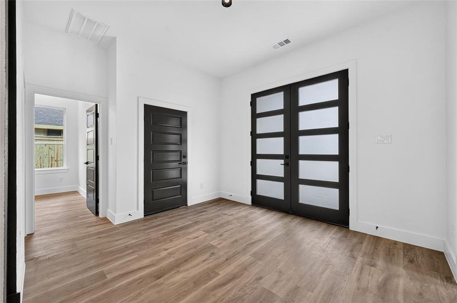 Spacious room featuring wood-finish flooring, white walls, and a pair of modern French doors with frosted glass panels Spacious room featuring wood-finish flooring, white walls, and a pair of modern French doors with frosted glass panels